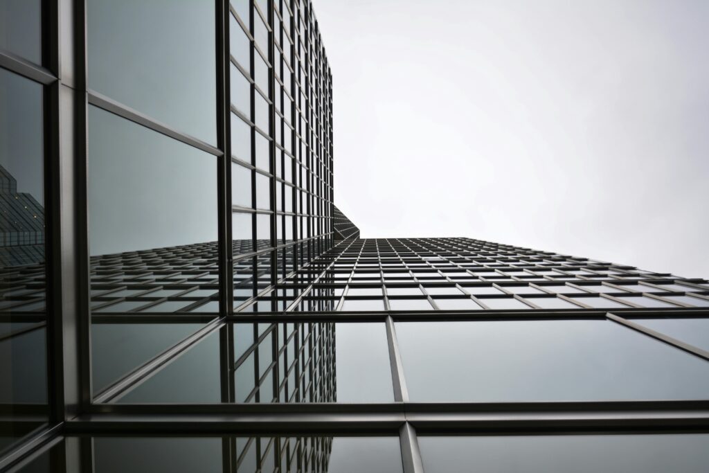 Low angle view of a modern glass skyscraper with reflective panels in an urban setting.